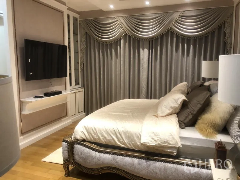 คอนโด ขายในWatthana, Bangkok - ห้องนอนหลักเตียงบุนุ่ม ชุดเครื่องนอนเงางาม ม่านหลุยส์ประดับหรู แสงไฟอบอุ่น และทีวีติดผนัง