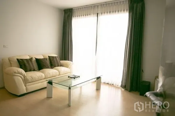 Condominium for rent in Watthana, Bangkok - Living room with cream sofa, glass coffee table and full-height curtained window.