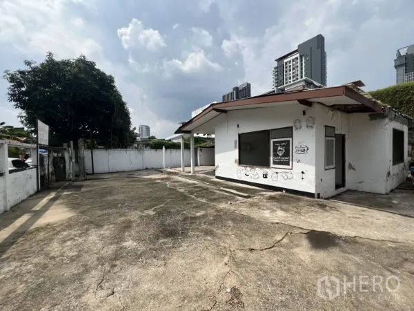 独立式住宅 出租在Phra Khanong, Bangkok - 房屋正面视角，白色小屋配超大混凝土车道与围墙庭院。