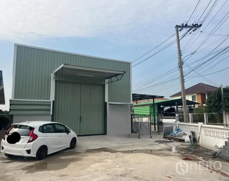 โกดัง for rent in Pak Kret, Nonthaburi - ด้านหน้าโกดังพร้อมประตูบานใหญ่ หลังคากันสาดโหลดสินค้า และลานคอนกรีต