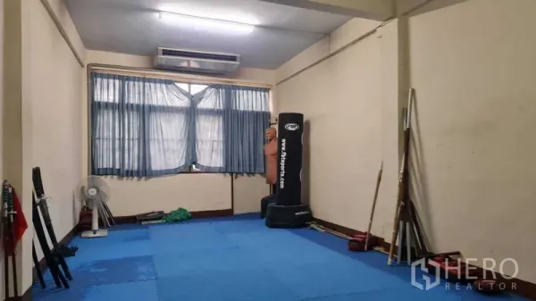 Shophouse for sale in Watthana, Bangkok - Upper-floor open room with window AC, blue training mats, and equipment.