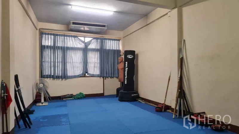 Shophouse for sale in Watthana, Bangkok - Upper-floor open room with window AC, blue training mats, and equipment.