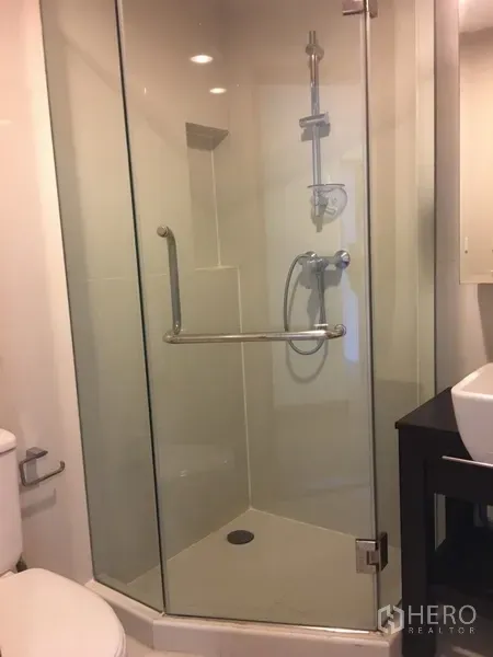 Condominium for rent in Pathum Wan, Bangkok - Bathroom with glass-enclosed corner shower, handheld shower, vanity and toilet.