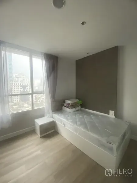 Condominium for rent in Pathum Wan, Bangkok - Bright bedroom with large window, city view, light wood floors and single bed in a Pathum Wan condo.