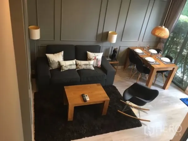 Condominium for rent in Phra Khanong, Bangkok - Cozy lounge with dark sofa, wooden coffee table, and window-side dining set