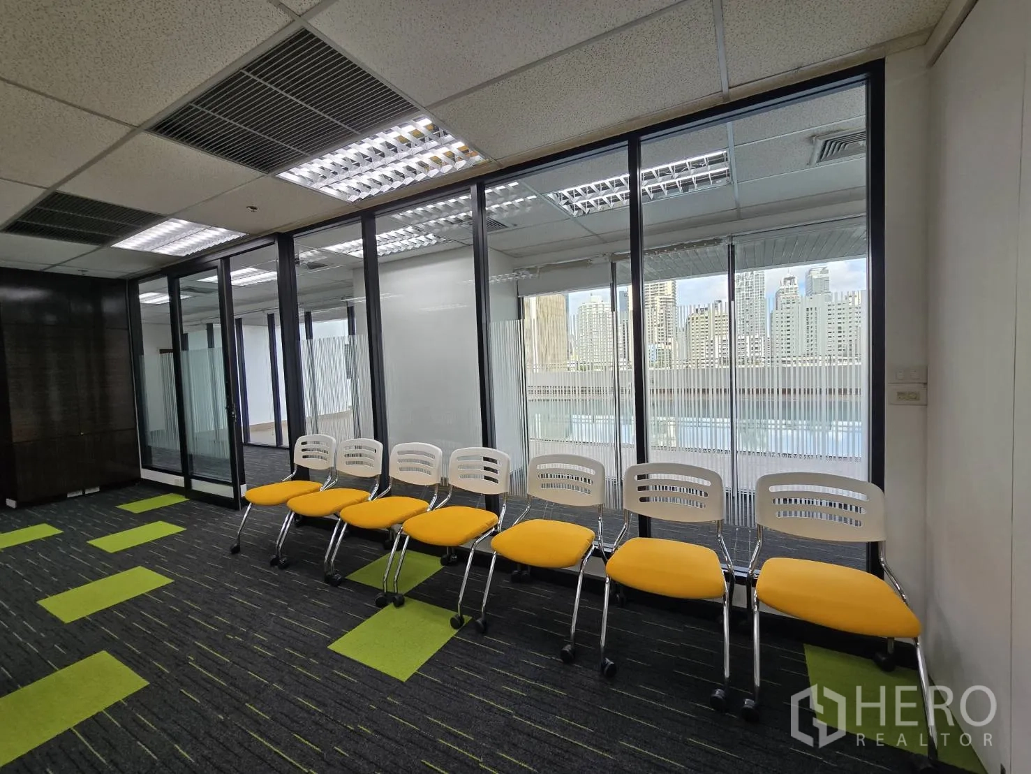 Office Space for rent in Watthana, Bangkok - Row of yellow chairs by a glass wall with skyline view.