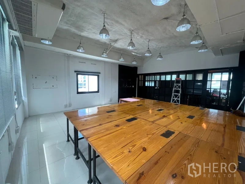 办公空间 出租在Khlong Toei, Bangkok - 开放式办公室，大片木质工位、吊灯、空调与黑色框架玻璃隔断。