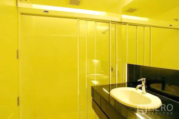 Condominium for rent in Watthana, Bangkok - Modern bathroom featuring a glass-enclosed shower, vanity with white basin and black countertop under soft lighting.