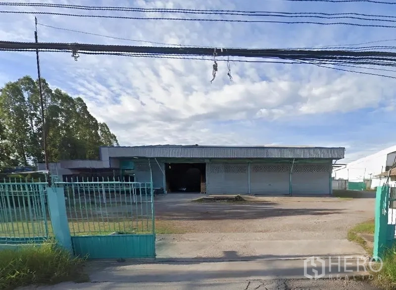 คลังสินค้า ให้เช่าในMueang Samut Sakhon, Samut Sakhon - ด้านหน้าโกดังอุตสาหกรรมพร้อมประตูรั้วและลานจอด ใต้ท้องฟ้าสีฟ้า
