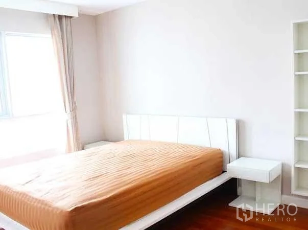 Condominium for rent in Huai Khwang, Bangkok - Bright bedroom with a large window, white bed frame, side tables and tall shelving.