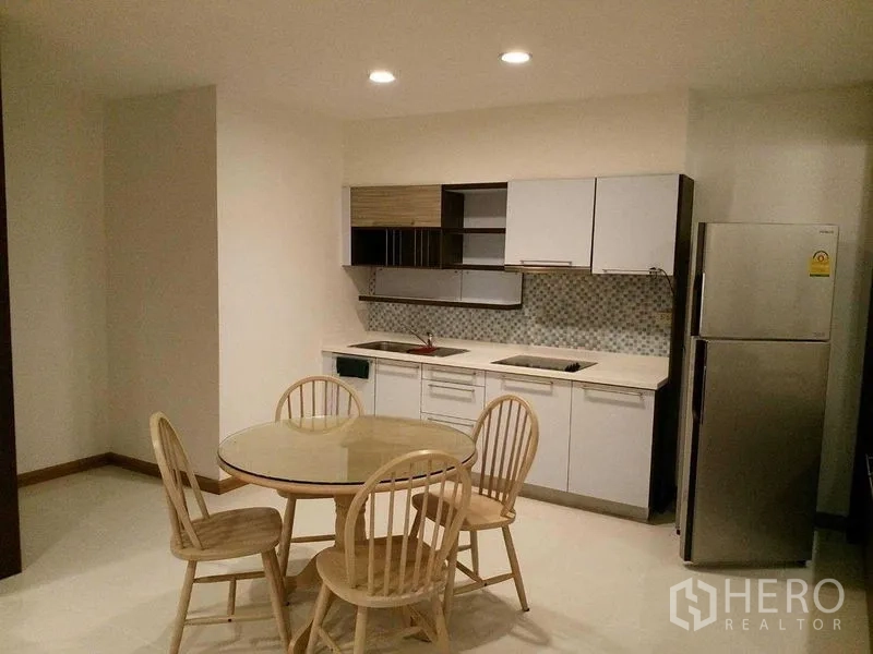 Condominium for rent in Sathon, Bangkok - Open kitchen with white cabinetry, mosaic backsplash, cooktop, refrigerator, and a round table with four chairs.