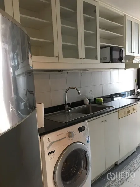Condominium for rent in Pathum Wan, Bangkok - Separate galley kitchen with white cabinets, black countertop, sink, washing machine and microwave.