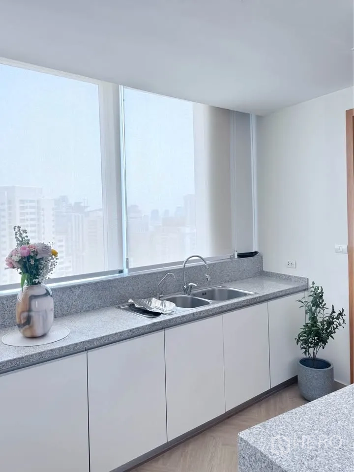 คอนโด for rent or sale in Khlong Toei, Bangkok - ครัวสว่างด้วยเคาน์เตอร์หินแกรนิตยาว อ่างล้างจานคู่ และหน้าต่างบานใหญ่เห็นวิวเมือง.