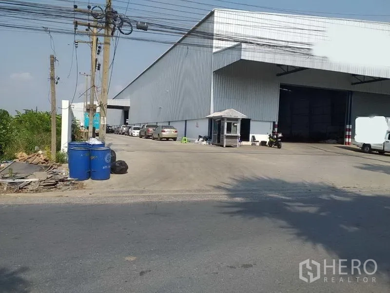 Warehouse for rent in Nonthaburi - Side view of a large industrial warehouse entrance with ample driveway and on‑site parking.
