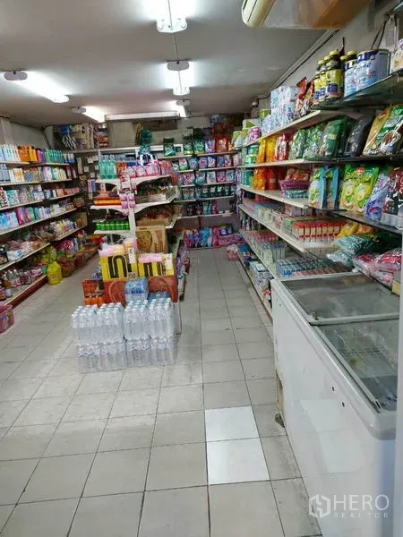 零售空间 出租在Bang Na, Bangkok - 明亮的零售店内部，瓷砖地面，中央通道，两侧货架摆满日用品与食品。