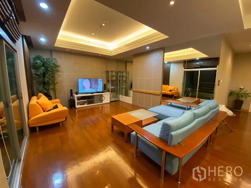 Condominium for rent in Pathum Wan, Bangkok - Spacious living room with recessed ceilings, wooden floors, TV and sliding doors to a balcony.