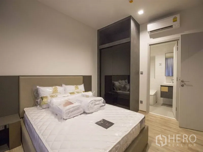 Condominium for rent in Chatuchak, Bangkok - Bedroom with upholstered headboard, built-in wardrobe, air conditioner, and door to ensuite bathroom.