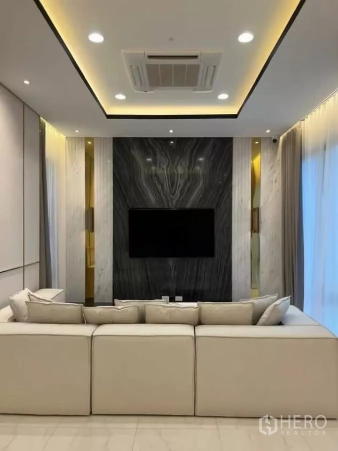 独立式住宅 出租在Phaya Thai, Bangkok - 电视背景墙为深色大理石，柔光照明与米色沙发。