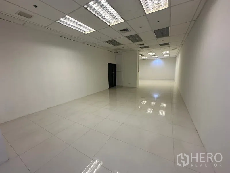 Office Space for rent in Ratchathewi, Bangkok - Deep rectangular room with white tile flooring and fluorescent ceiling lights.