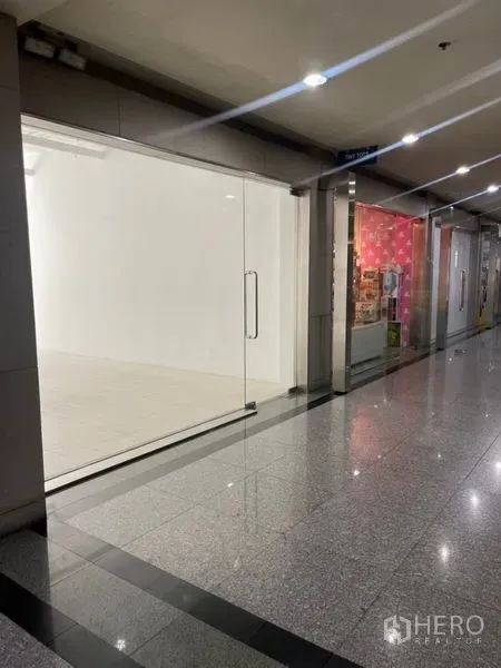 零售空间 出租在Khlong Toei, Bangkok - 商场走廊视角的空置店铺，落地玻璃门面一览无遗。