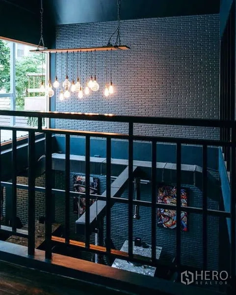 独立式住宅 出租在Watthana, Bangkok - 挑高中庭平台，吊灯、金属栏杆与砖墙景观，可见窗外绿意。