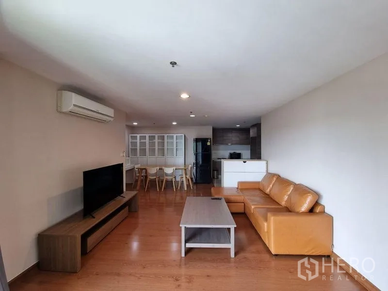 Condominium for rent in Huai Khwang, Bangkok - Wide living room featuring a tan leather sofa, TV unit and open-plan kitchen.