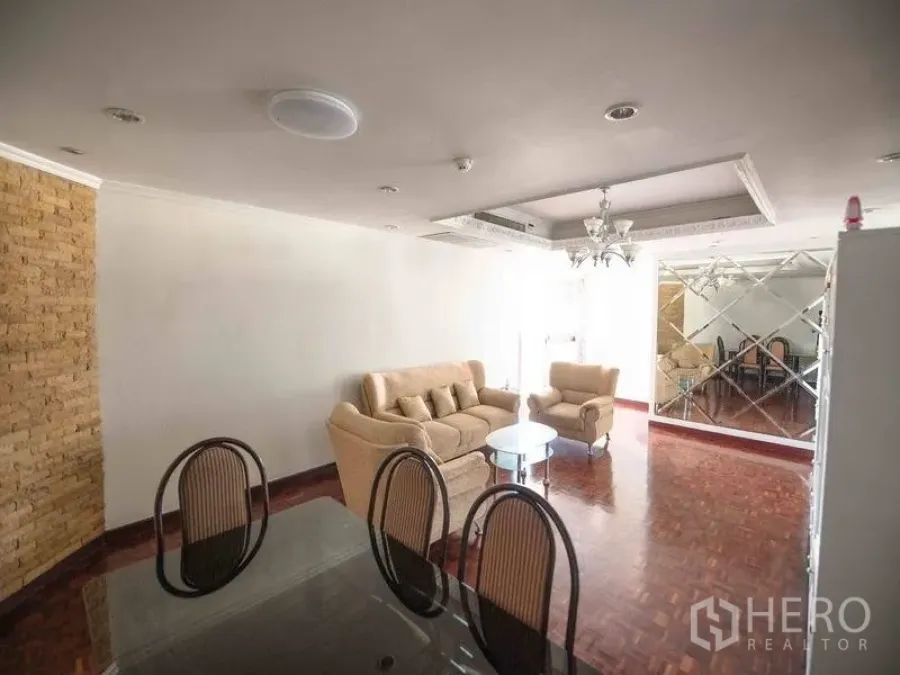 Condominium for rent in Watthana, Bangkok - Bright living and dining area with parquet floors, beige sofas, chandelier, and a mirrored feature wall.