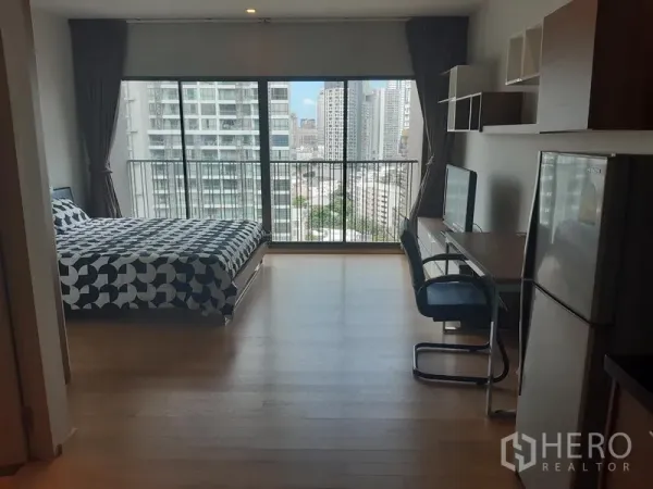 คอนโด ให้เช่าในBangkok - สตูดิโอสว่างโปร่ง มีหน้าต่างเต็มผนัง เตียง โต๊ะทำงาน และวิวเมืองจากระเบียง