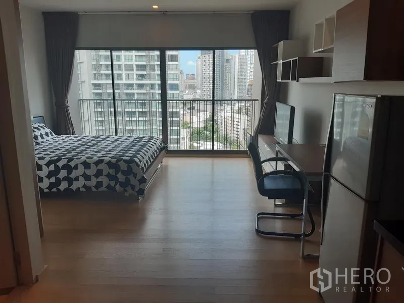 คอนโด ให้เช่าในBangkok - สตูดิโอสว่างโปร่ง มีหน้าต่างเต็มผนัง เตียง โต๊ะทำงาน และวิวเมืองจากระเบียง