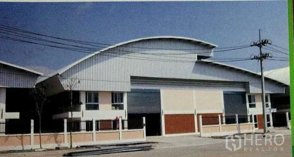 工厂 出租在Ban Phaeo, Samut Sakhon - 工厂外观，弧形金属屋顶与大型卷帘门，临街围栏整齐。