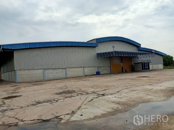 Factory for rent in Chaloem Phra Kiat, Saraburi - Front view of large warehouse factory with wide entry doors and extensive truck yard.