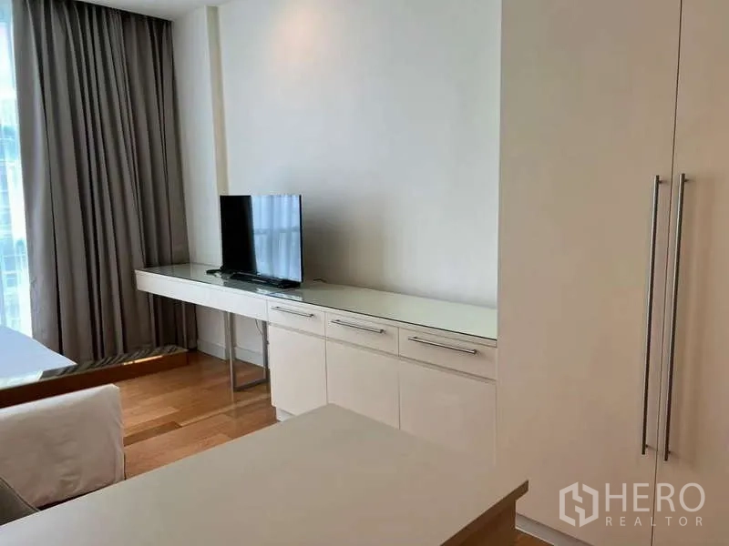 Condominium for rent in Bang Kho Laem, Bangkok - Bedroom cabinet wall with TV and long console under window drapes.