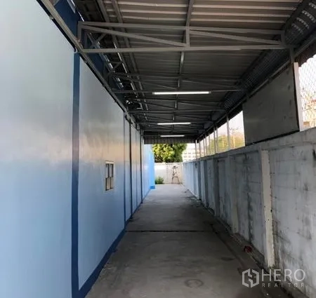 Factory for rent in Pathum Thani - Covered side walkway beside the factory with metal roof and concrete path.