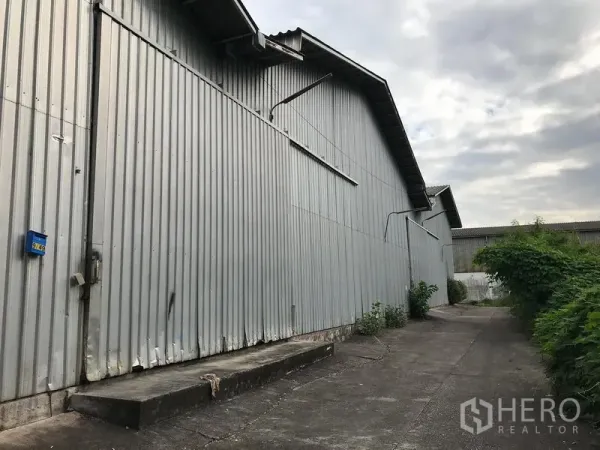 Warehouse for rent in Samut Prakan - Corrugated metal warehouse exterior with side driveway and a raised loading platform.