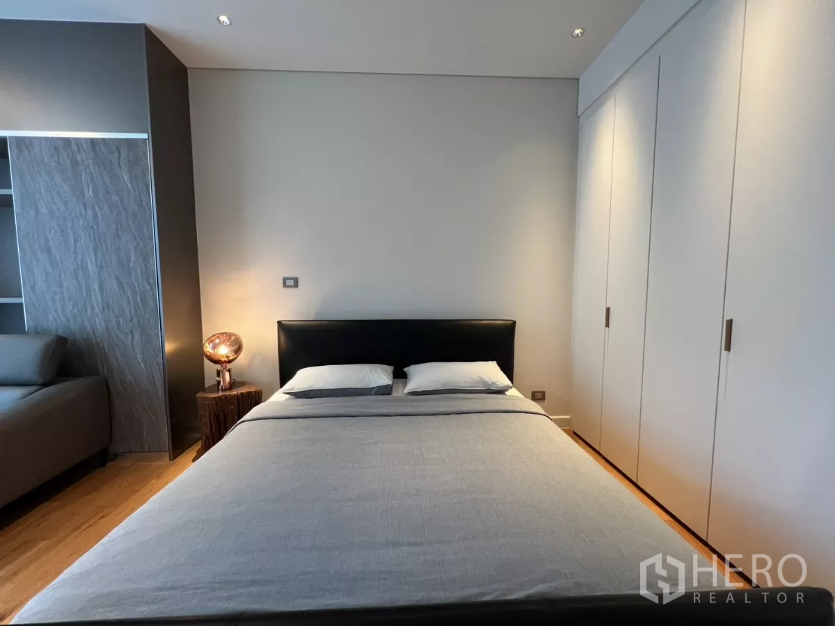 คอนโด ให้เช่าในPathum Wan, Bangkok - ห้องนอนสไตล์มินิมอล เตียงบุหนัง โคมไฟหัวเตียง และตู้เสื้อผ้าบิวต์อินสีขาว