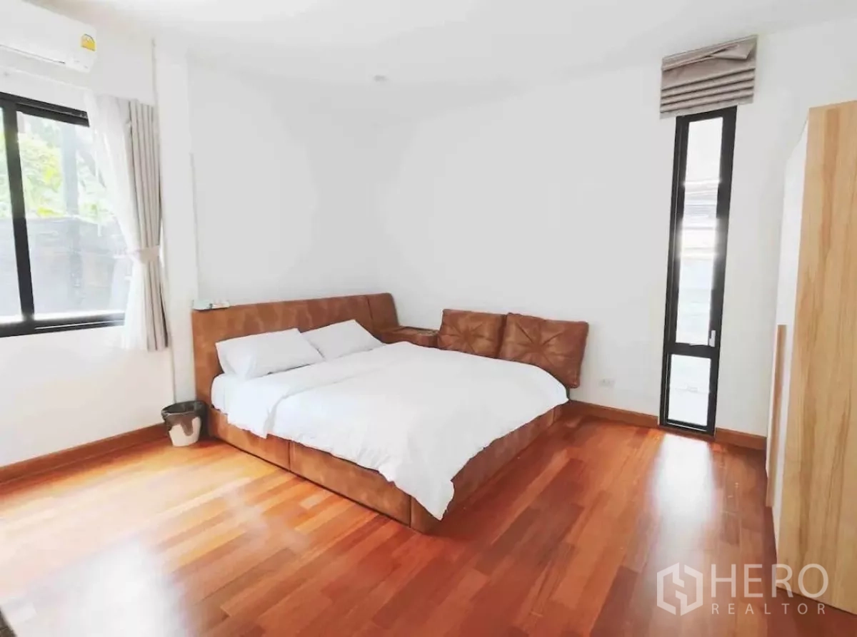 独立式住宅 出租在Phaya Thai, Bangkok - 温馨卧室，棕色皮床、木地板与高窄窗。