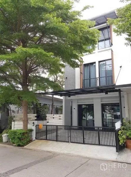 Townhouse for rent in Suan Luang, Bangkok - Three-storey modern townhouse facade in Suan Luang with gated carport and a large shade tree.