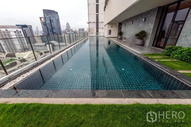 Condominium for rent in Watthana, Bangkok - High-floor lap pool with glass railing and city outlook beside landscaped deck.