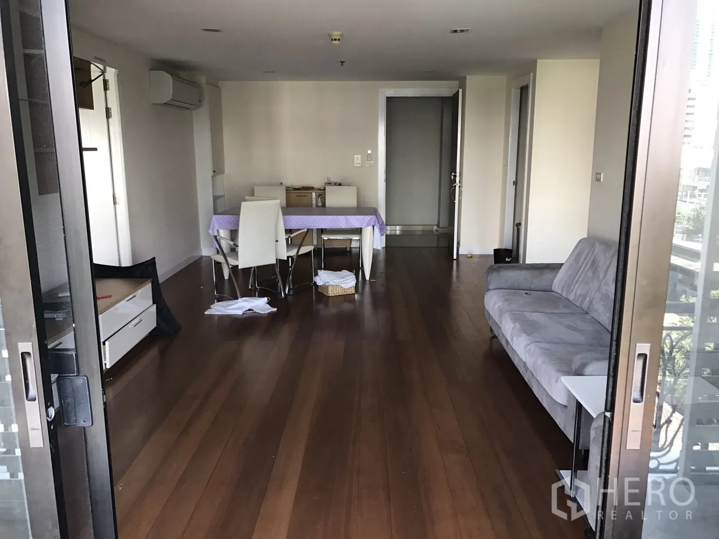 คอนโด ให้เช่าหรือขายในWatthana, Bangkok - ห้องนั่งเล่นแบบโอเพ่นมีพื้นไม้ โซฟาสีเทาและชุดทานอาหาร มุมมองจากระเบียง.