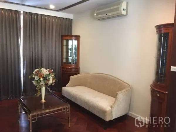 Detached House for rent in Bang Phli, Samut Prakan - Cozy sitting room featuring a cream sofa, glass coffee table, display cabinets, and blackout curtains.