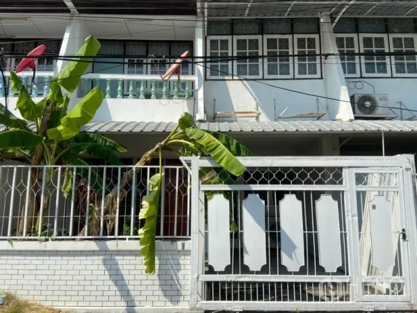 Townhouse for rent in Watthana, Bangkok - Two-storey townhouse facade with white metal gate, balcony and banana trees.