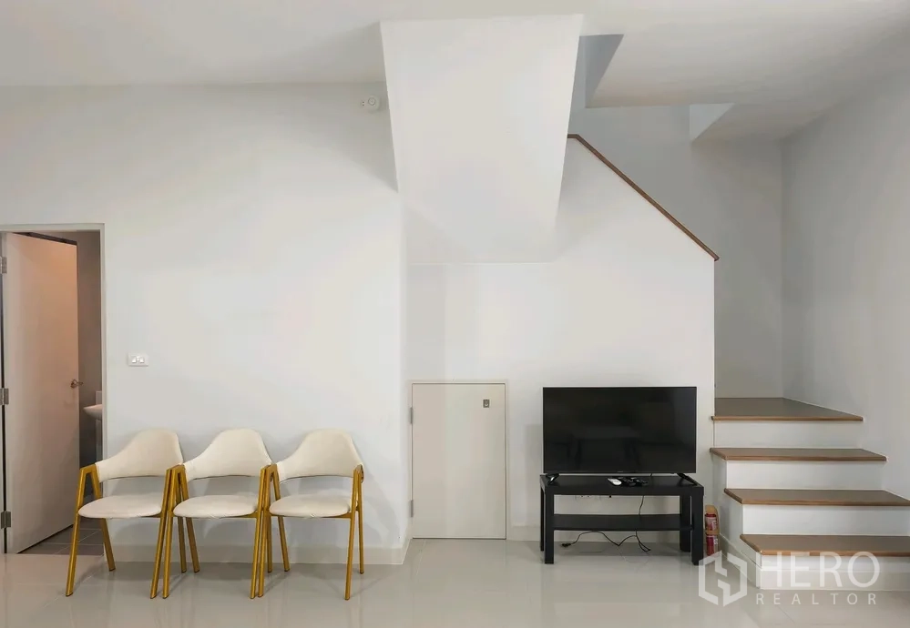Townhouse for rent in Bang Phli, Samut Prakan - TV area under the staircase with three chairs and a small storage door.