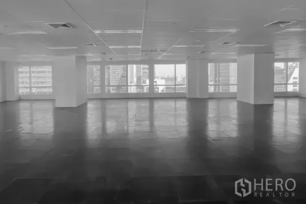 Office Space for rent - Large open-plan office floor with grid ceiling, lighting, AC vents, and wide windows showing Bangkok city views.