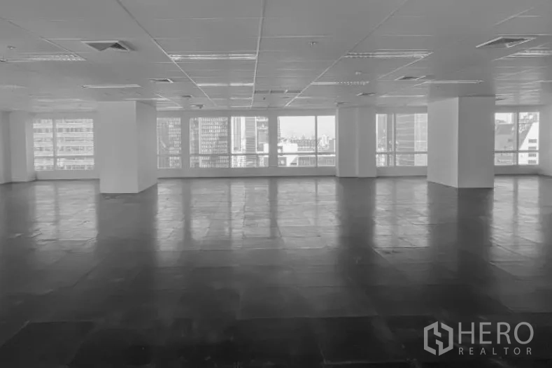 Office Space for rent - Large open-plan office floor with grid ceiling, lighting, AC vents, and wide windows showing Bangkok city views.