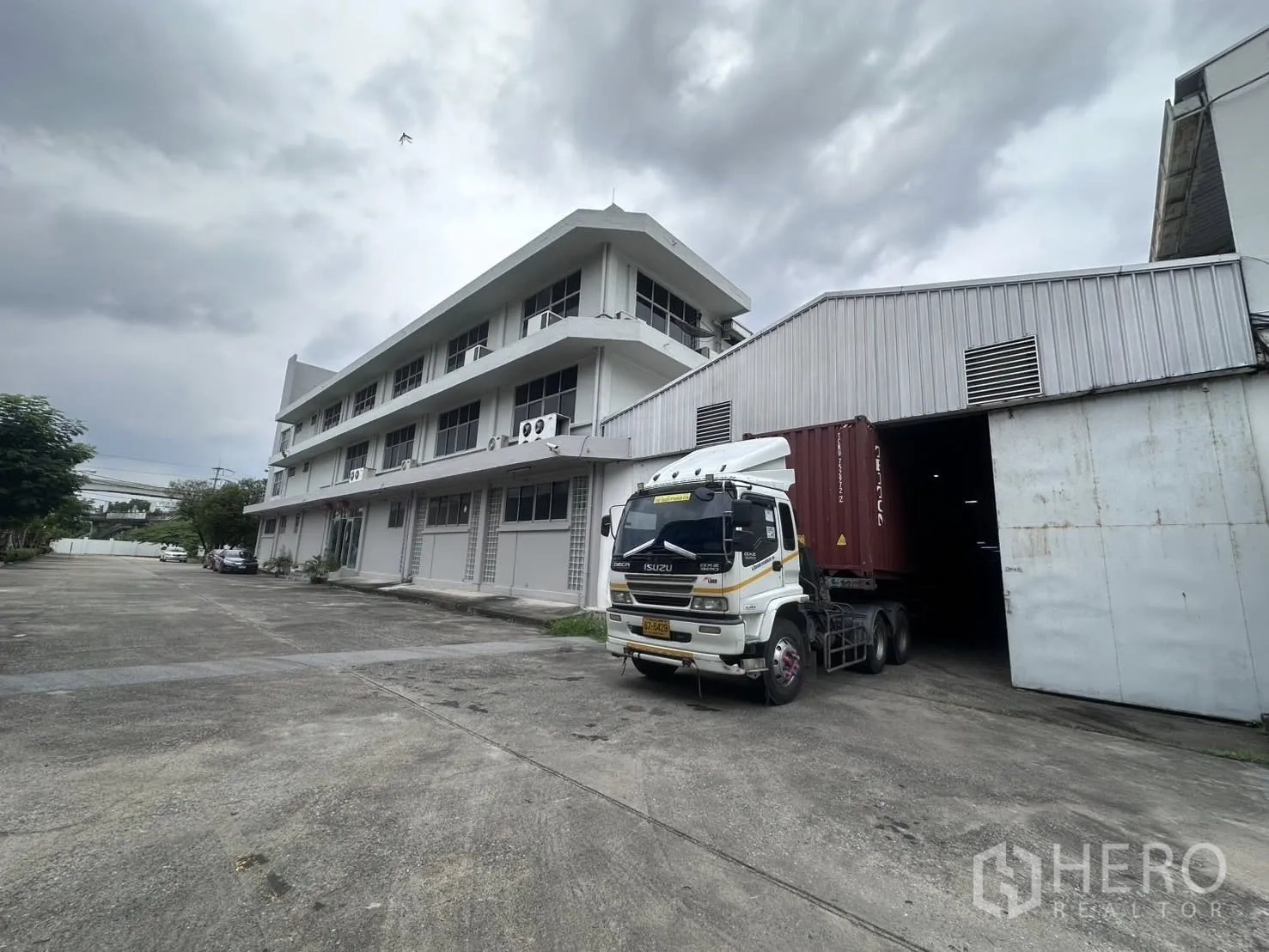 คลังสินค้า for rent in Mueang Samut Prakan, Samut Prakan - รถบรรทุกตู้คอนเทนเนอร์จอดที่ช่องโหลดข้างอาคารสำนักงานในวันที่ท้องฟ้าครึ้ม