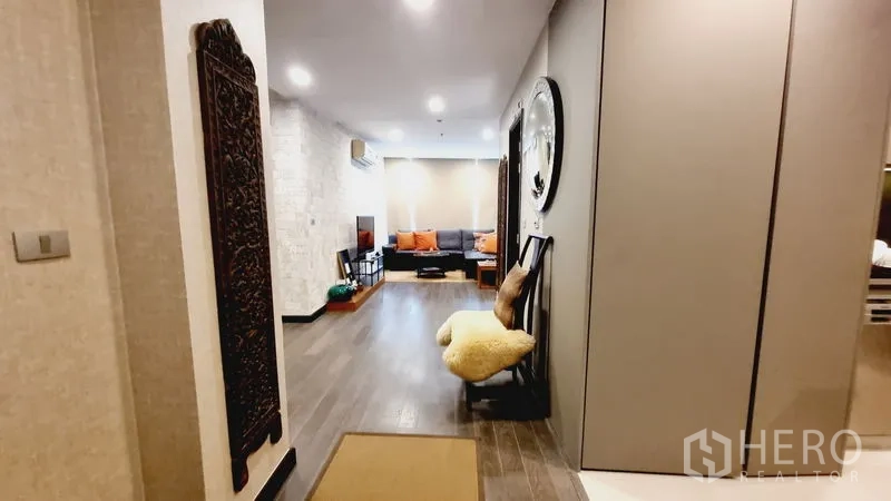 公寓 出售在Watthana, Bangkok - 入口走廊通向温馨客厅，木地板与墙面装饰画相映成趣。