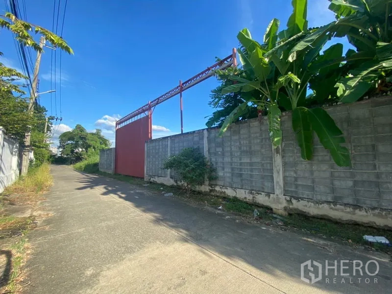 货栈 出租在Suan Luang, Bangkok - 静巷一侧的高围墙与大型红色滑动大门，为仓库出入口。