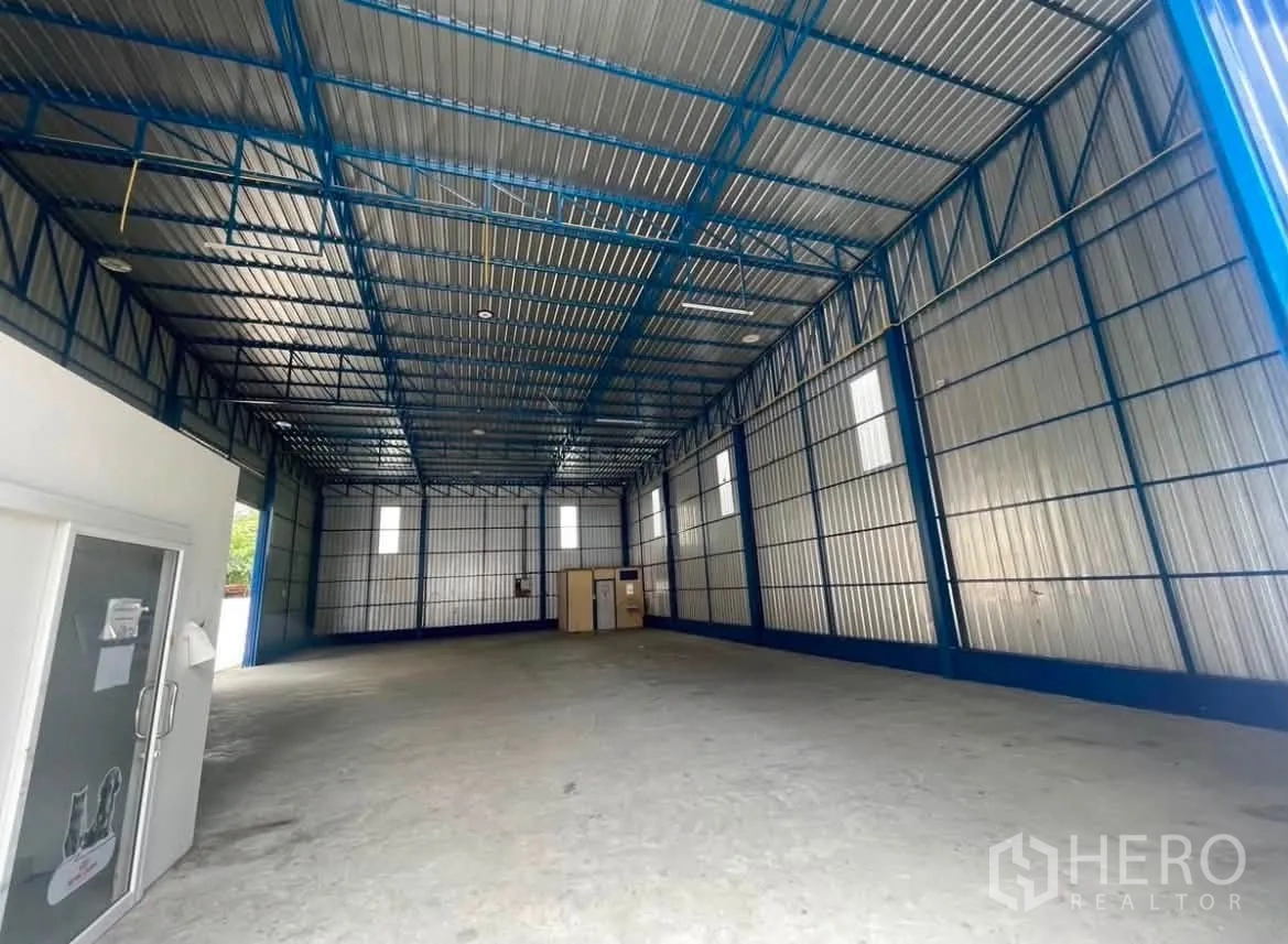 Warehouse for rent in Wang Thonglang, Bangkok - Open storage area with tall walls, high windows, and an enclosed room with a sink at the back.