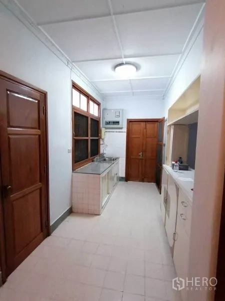 Detached House for rent in Pathum Wan, Bangkok - Galley kitchen with stainless sink, tiled counters and wooden doors.
