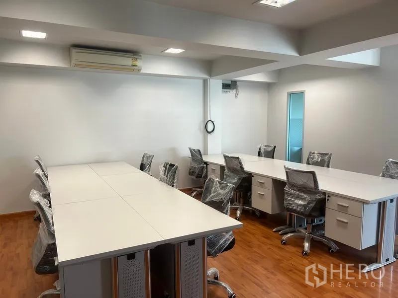 Office Space for rent in Khlong Toei, Bangkok - Open-plan office with long white worktables, wheeled chairs, wood floors and recessed lighting.